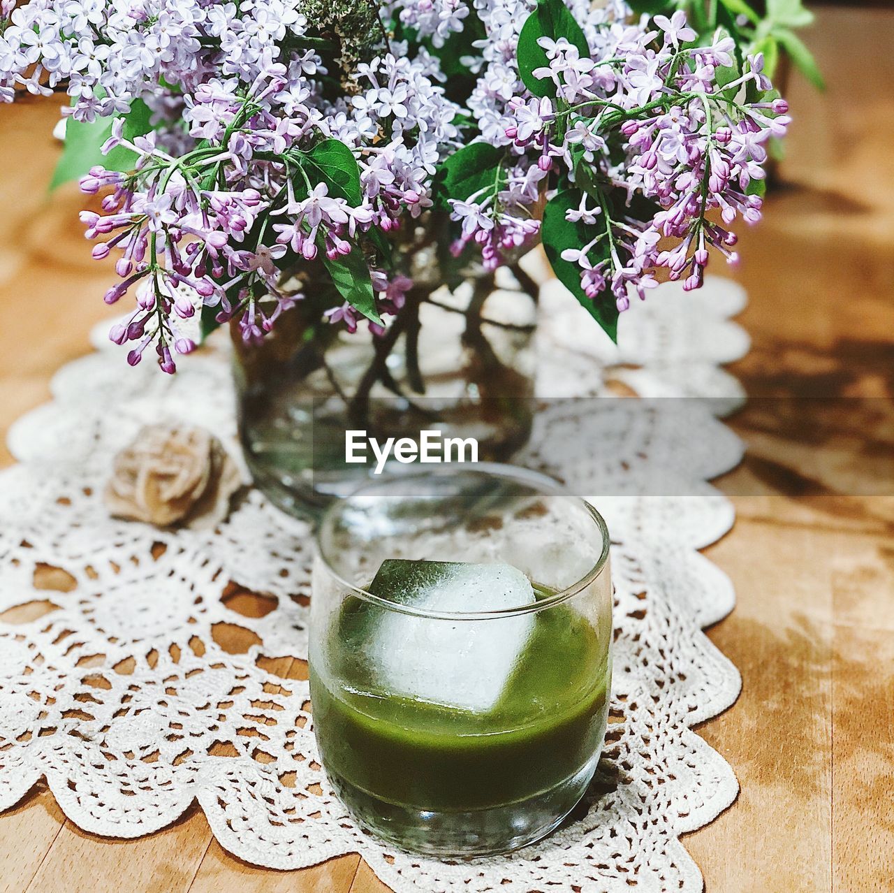 Close-up of green cocktail and vase with flowers on table