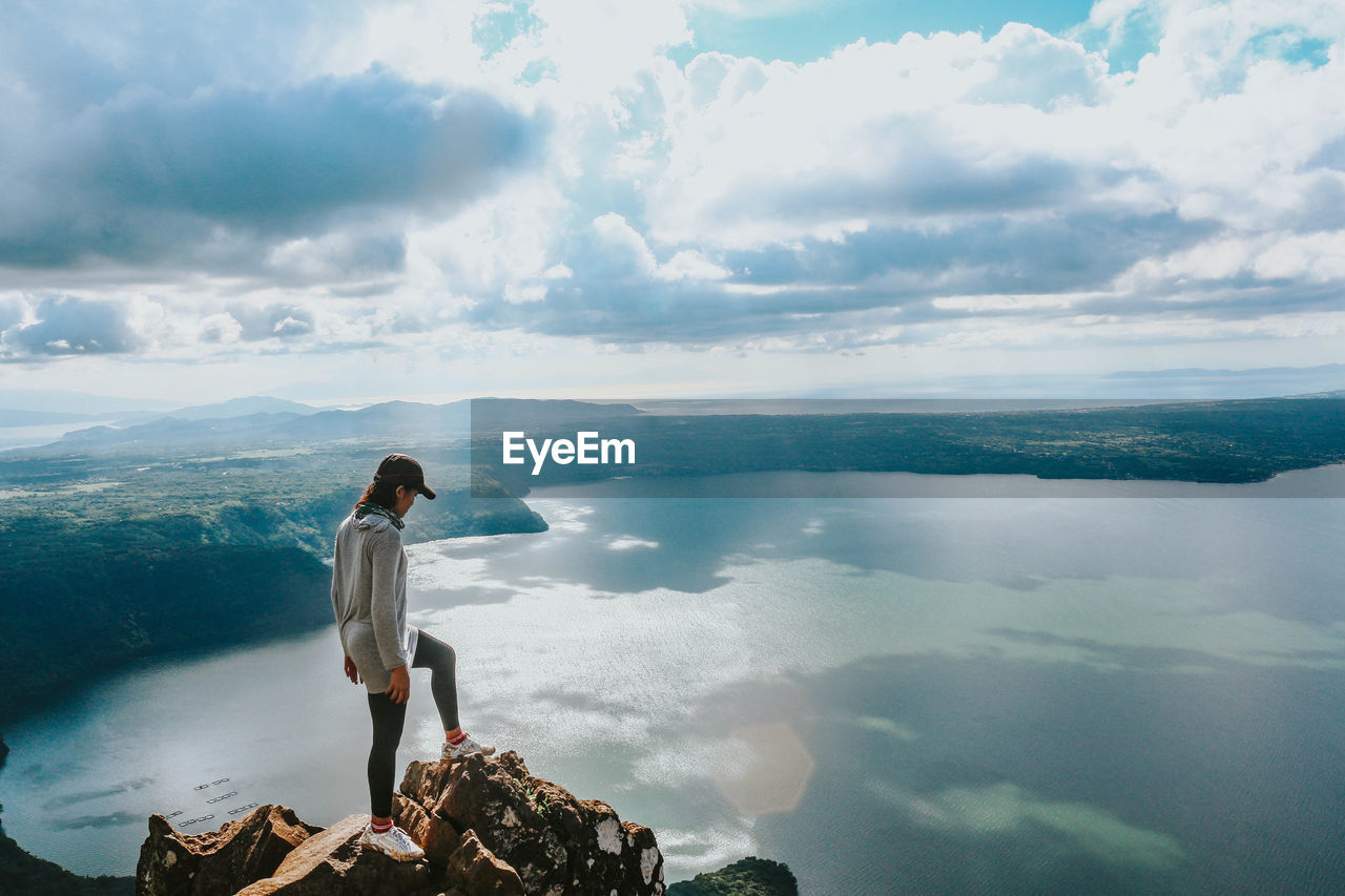 Woman standing on cliff by sea against sky