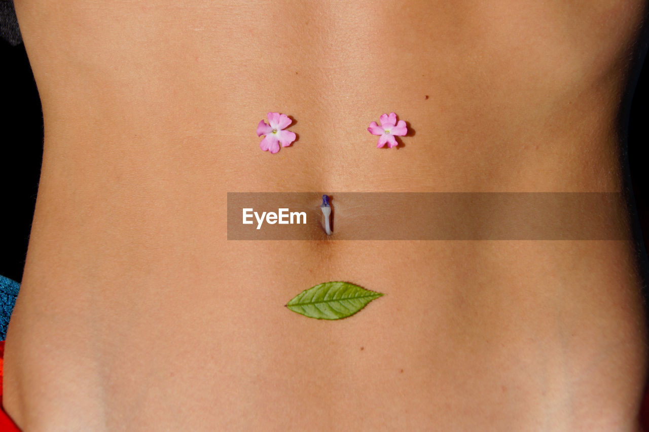 Midsection of woman with flowers and leaf on abdomen