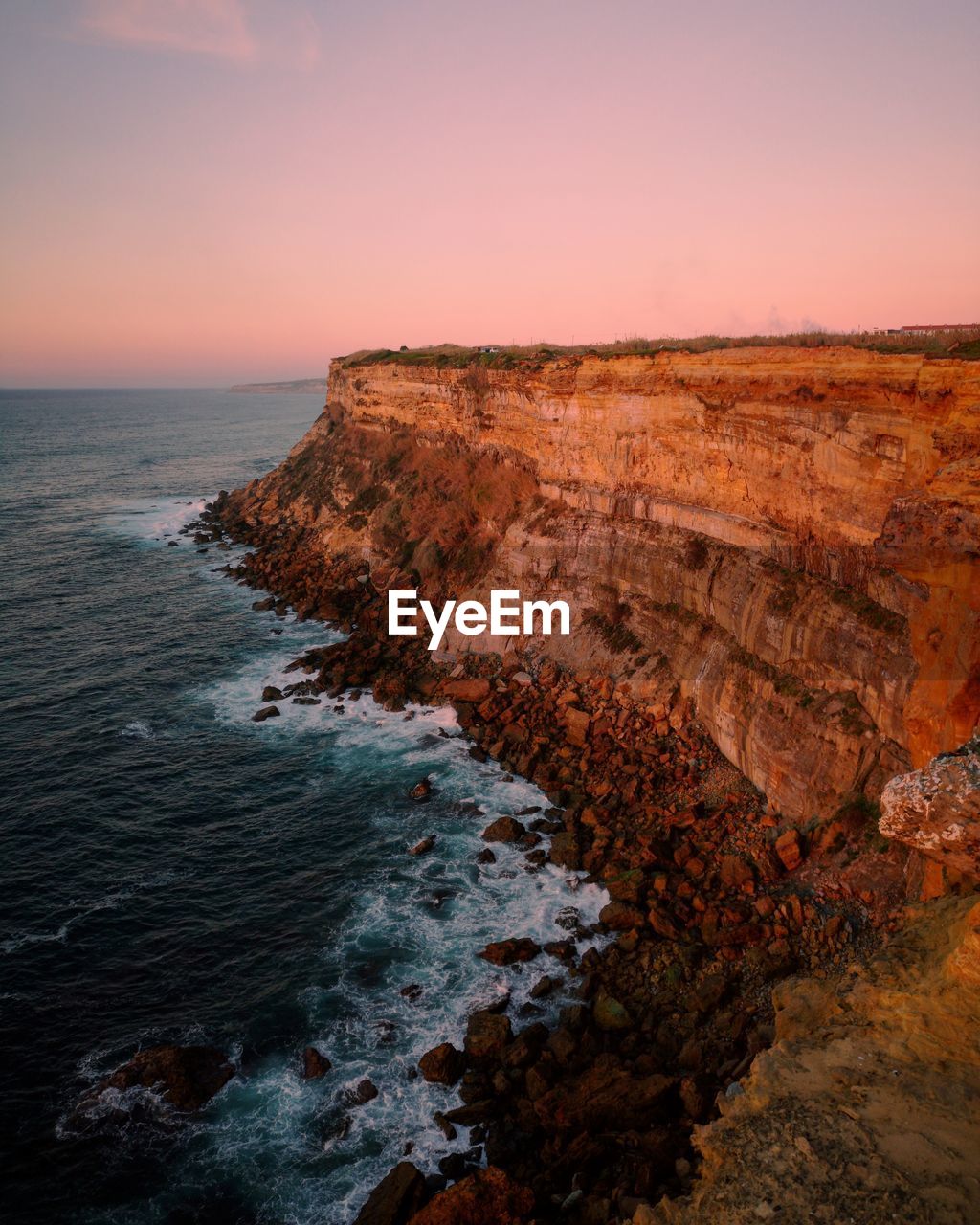 Scenic view of cliff by sea against sky during sunset