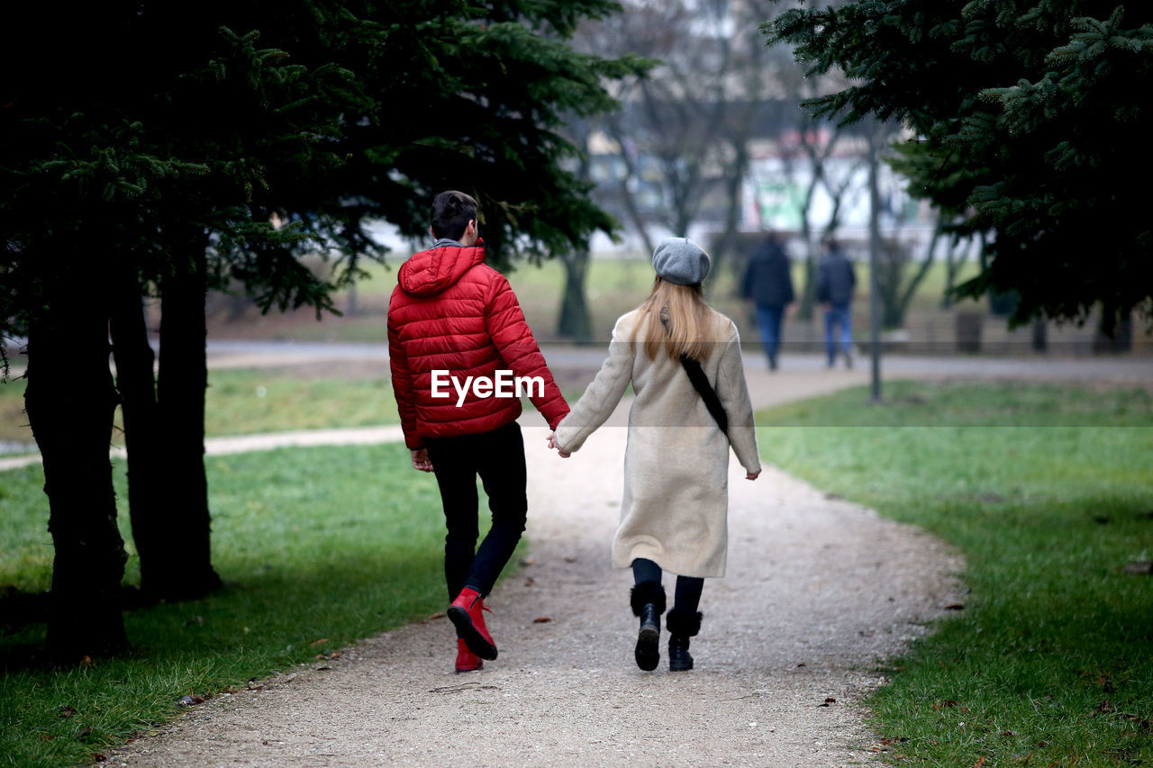 Rear view of couple holding hands walking on footpath at park