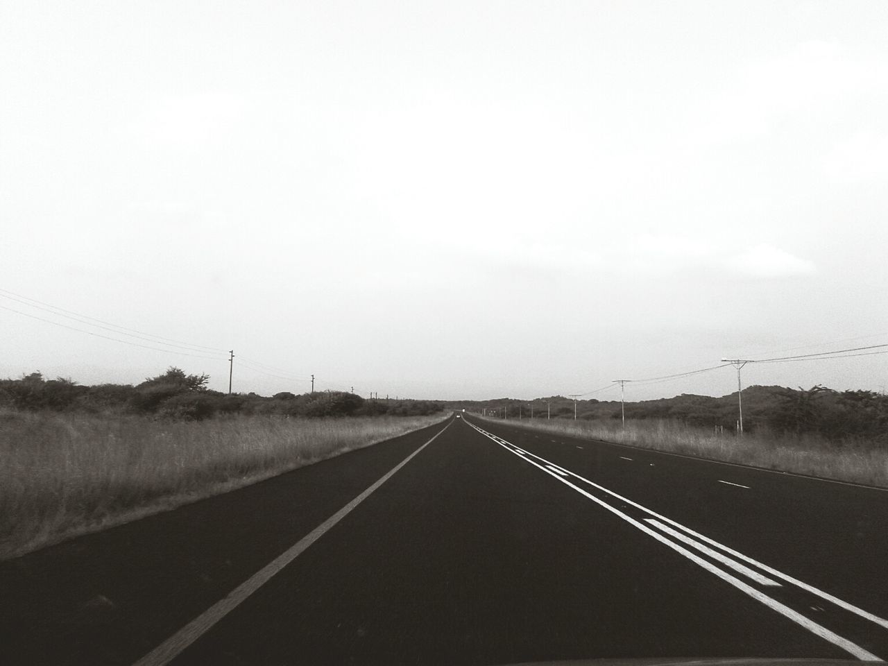 Empty road amidst field against sky