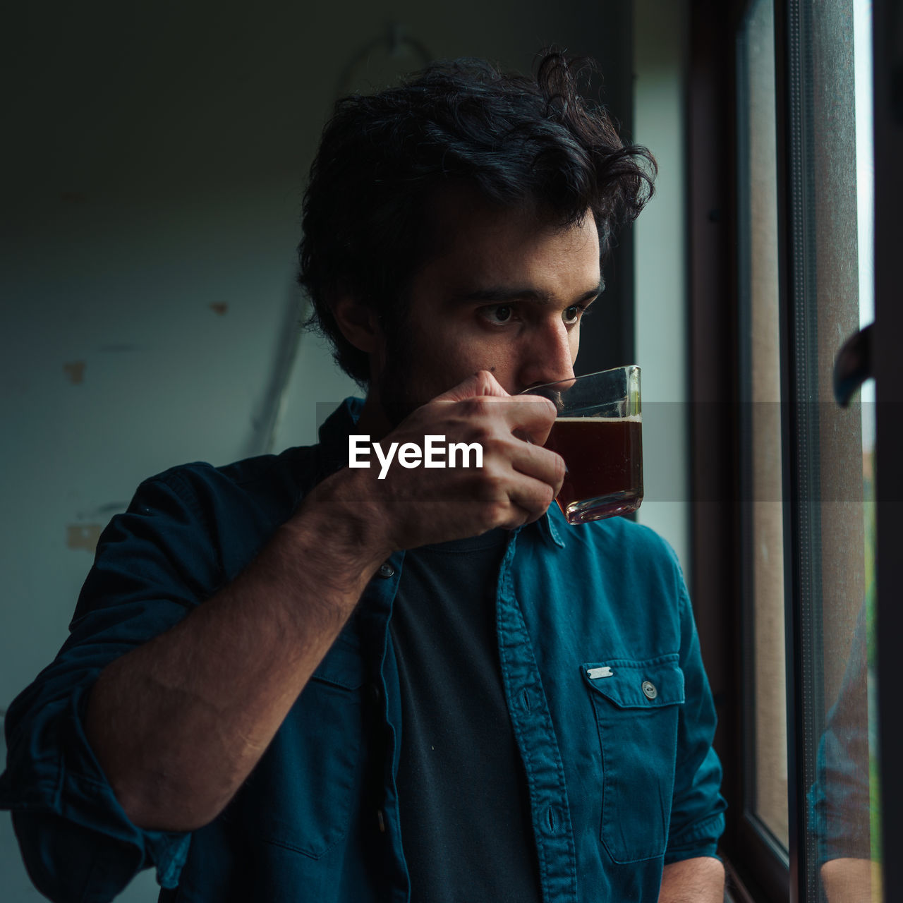 Man drinking tea while looking through window