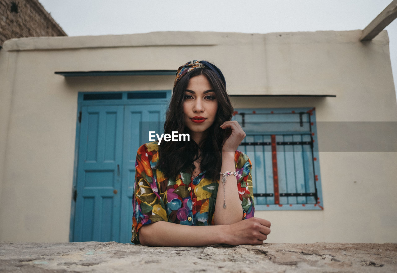 PORTRAIT OF YOUNG WOMAN AGAINST HOUSE
