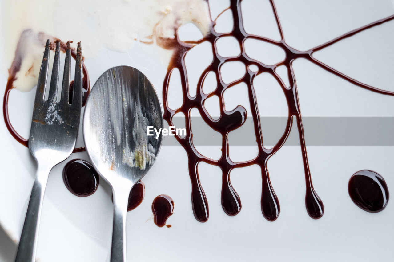 High angle view of fork and spoon on plate with chocolate sauce