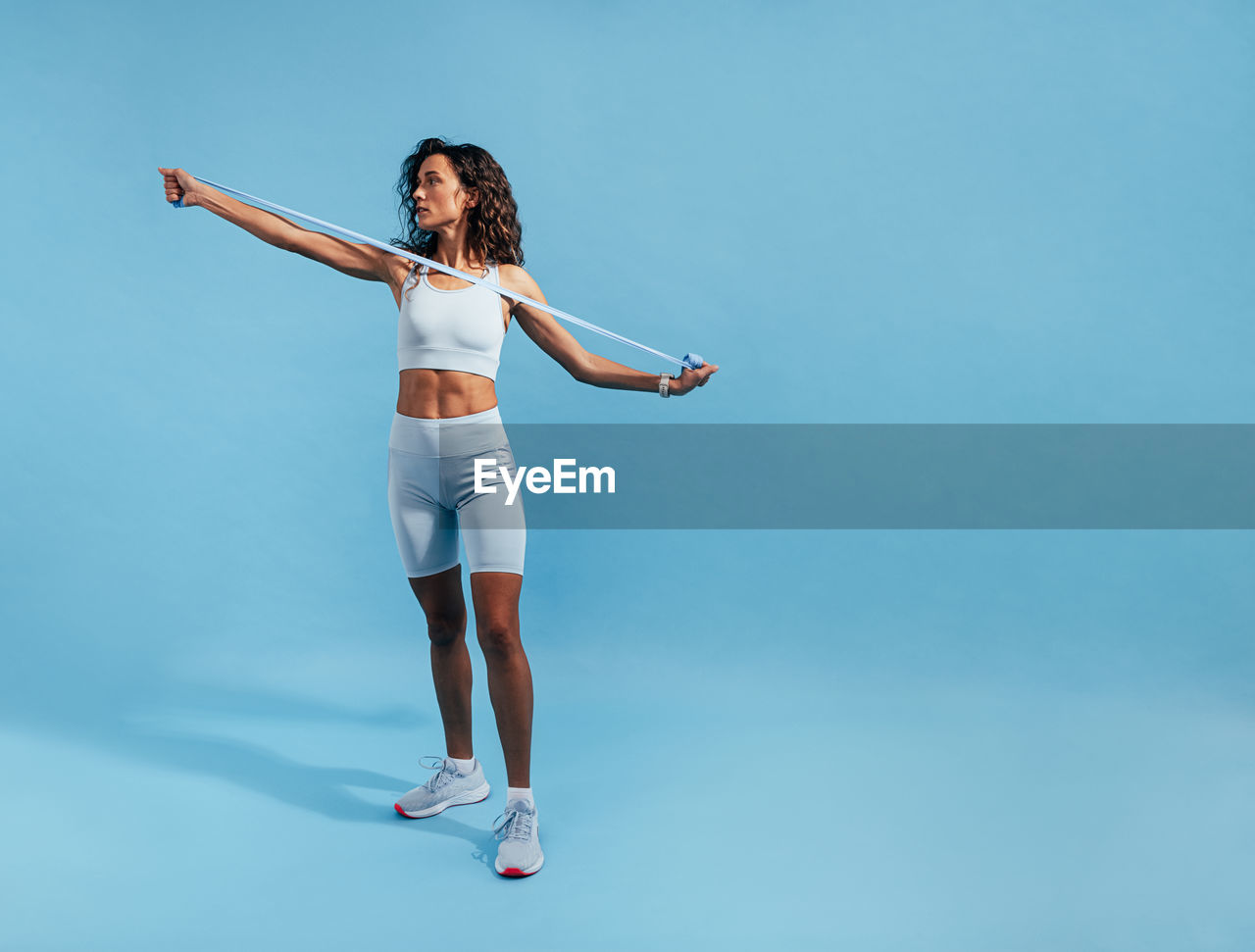 Full length of young woman exercising against blue background