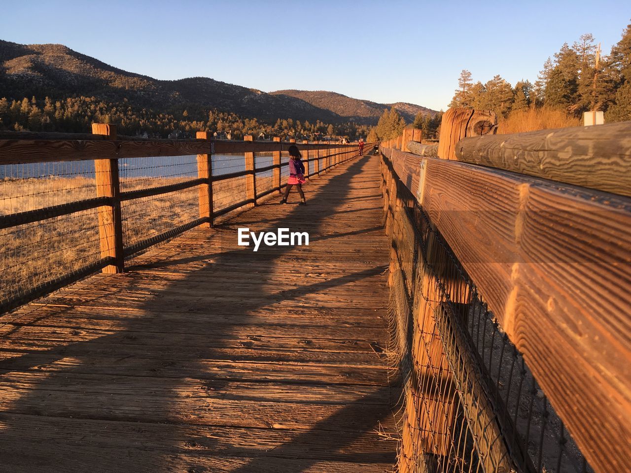 Girl walking on footbridge against clear sky