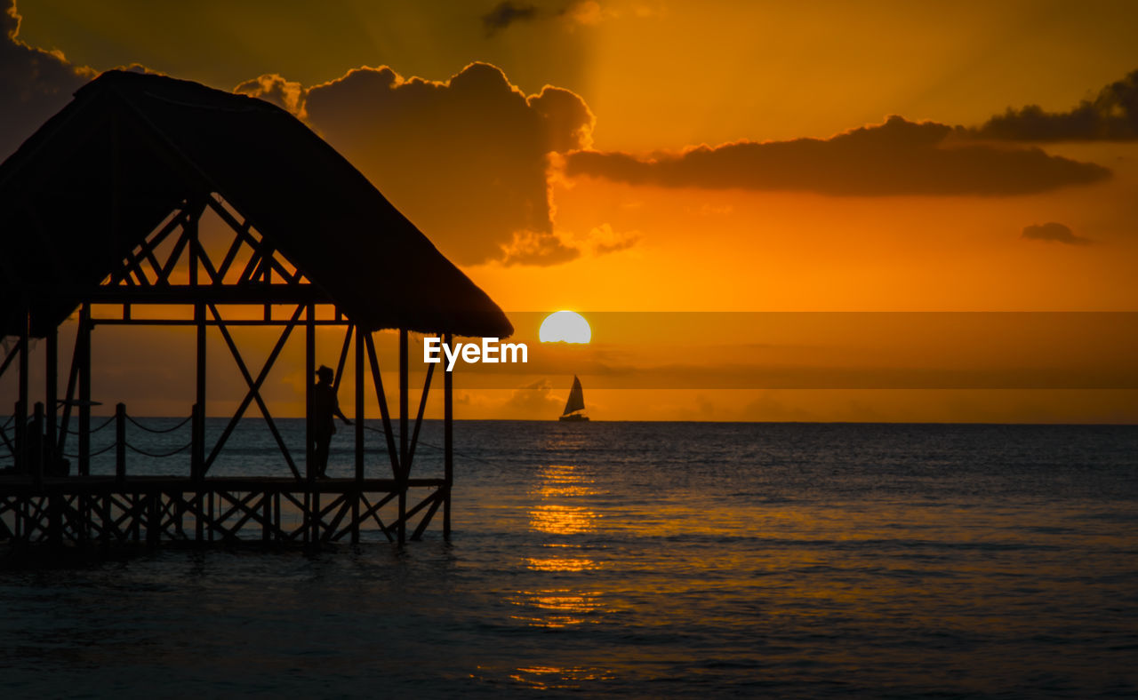 Silhouette person in gazebo fishing by sea during sunset