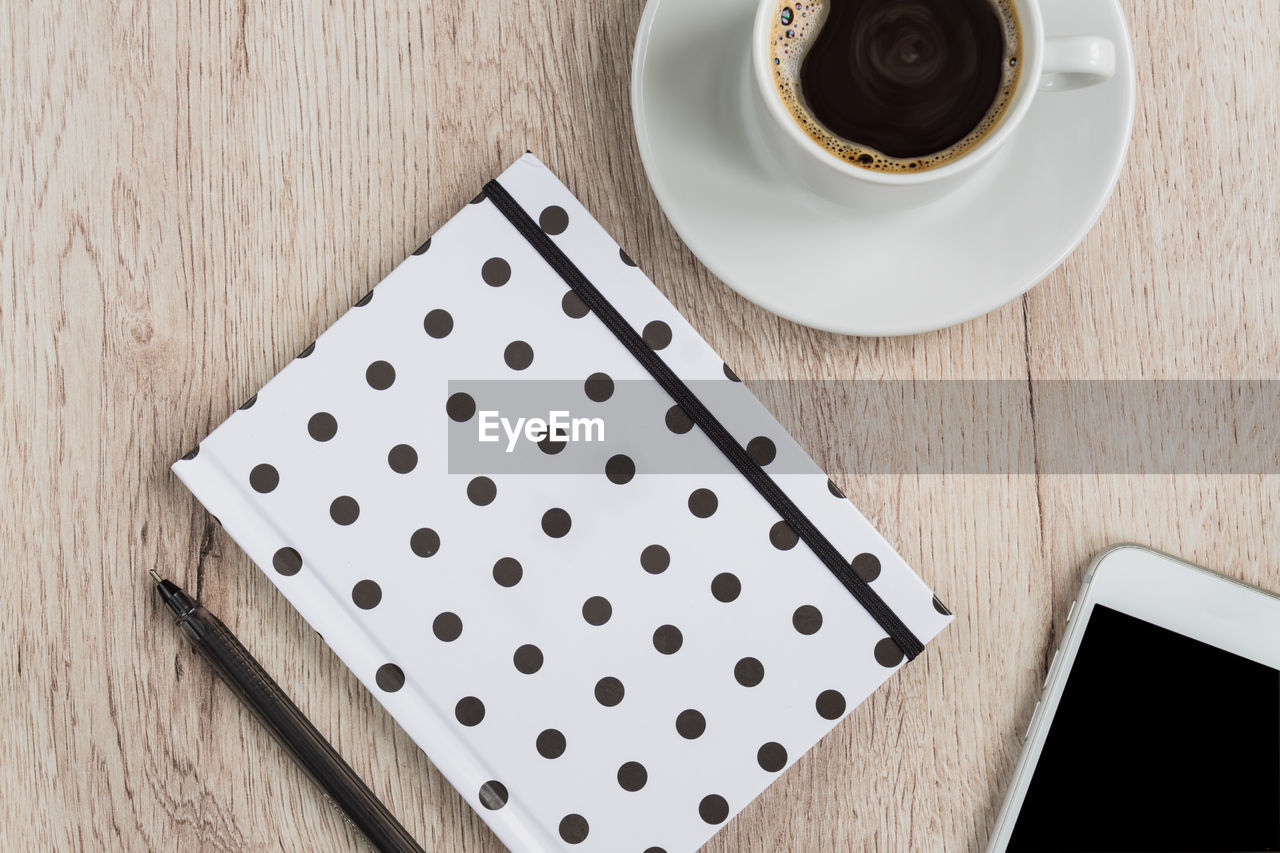 Business concept black and white polka dot cover notebook, smartphone and cup of black coffee