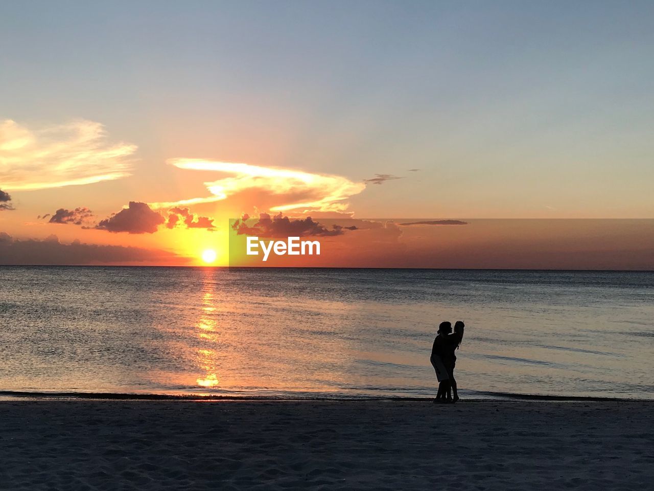 Couple embracing at beach against sky during sunset