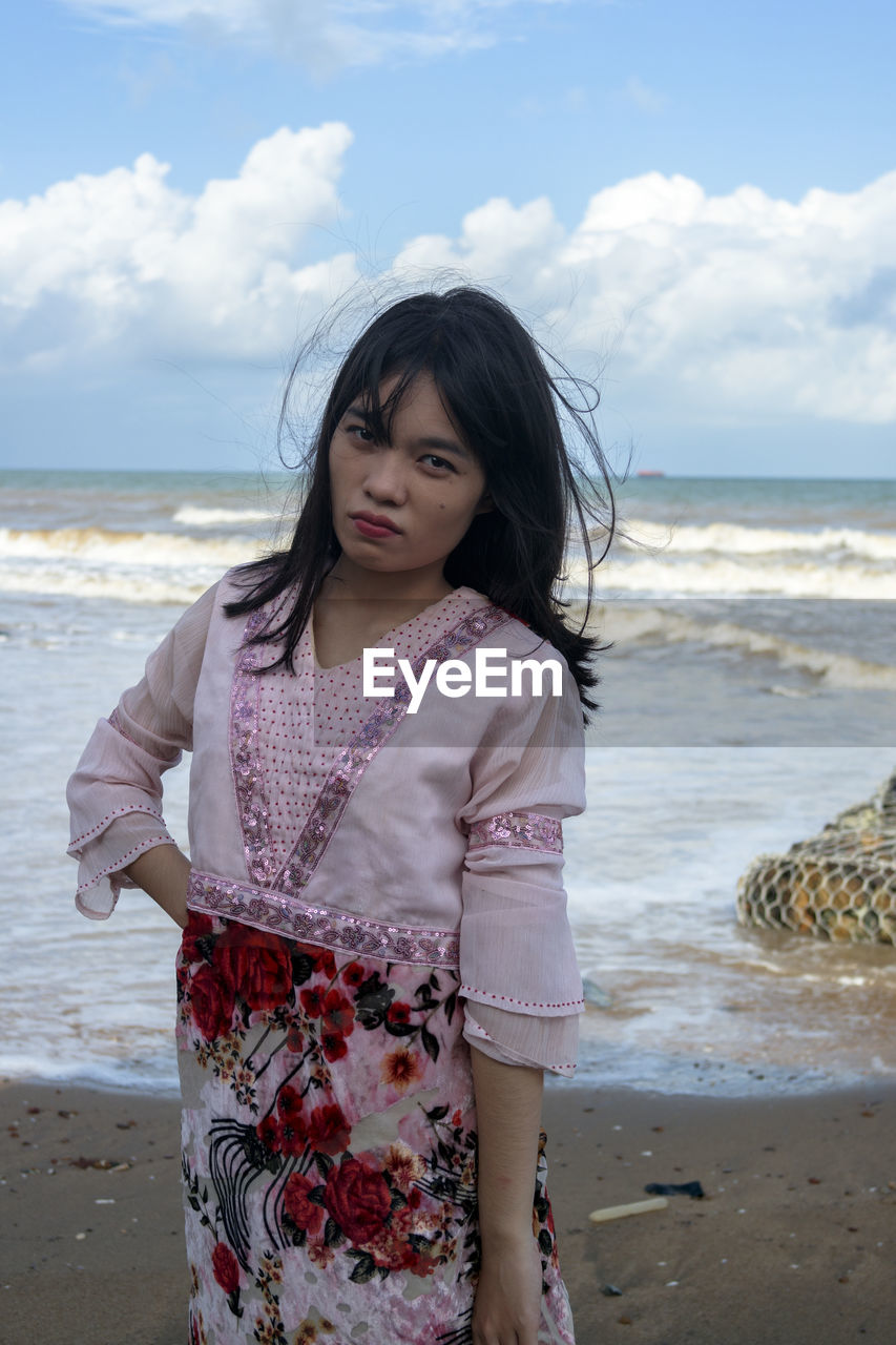 Beautiful woman standing at beach against sky