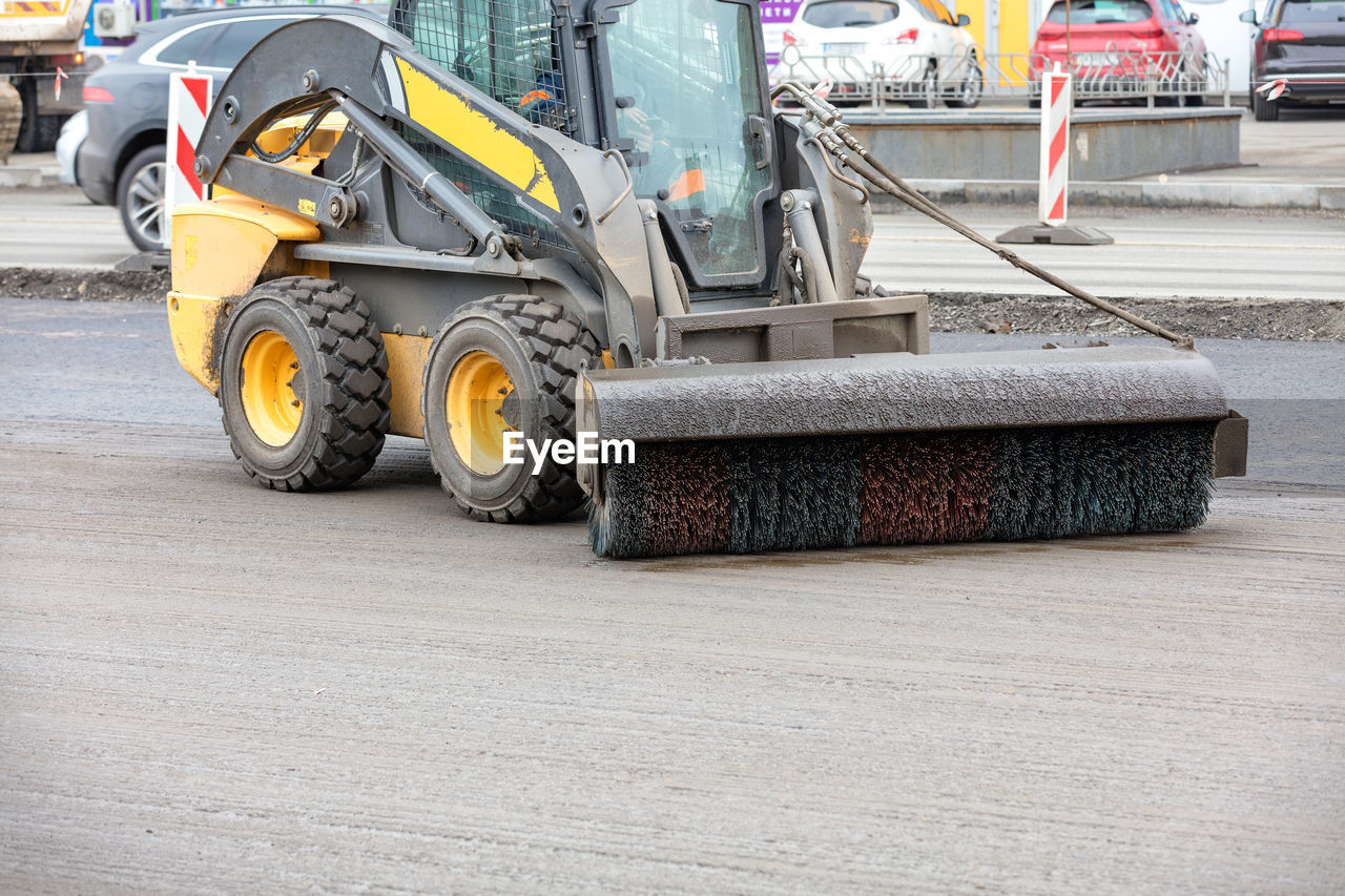 A small road grader with a nylon broom attached cleans the dirt from the asphalt roadbed.