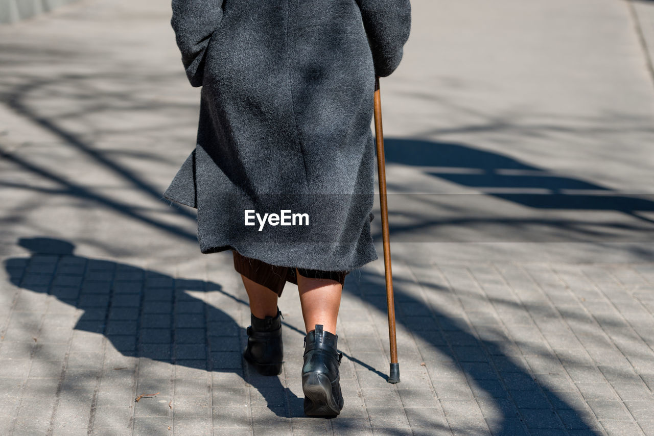 Low section of woman with cane walking on footpath