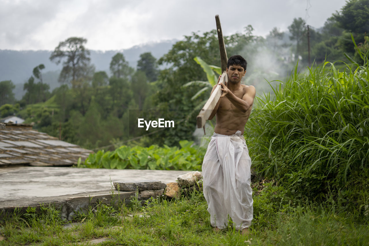 Happy indian farmer standing with wooden plough in rice field