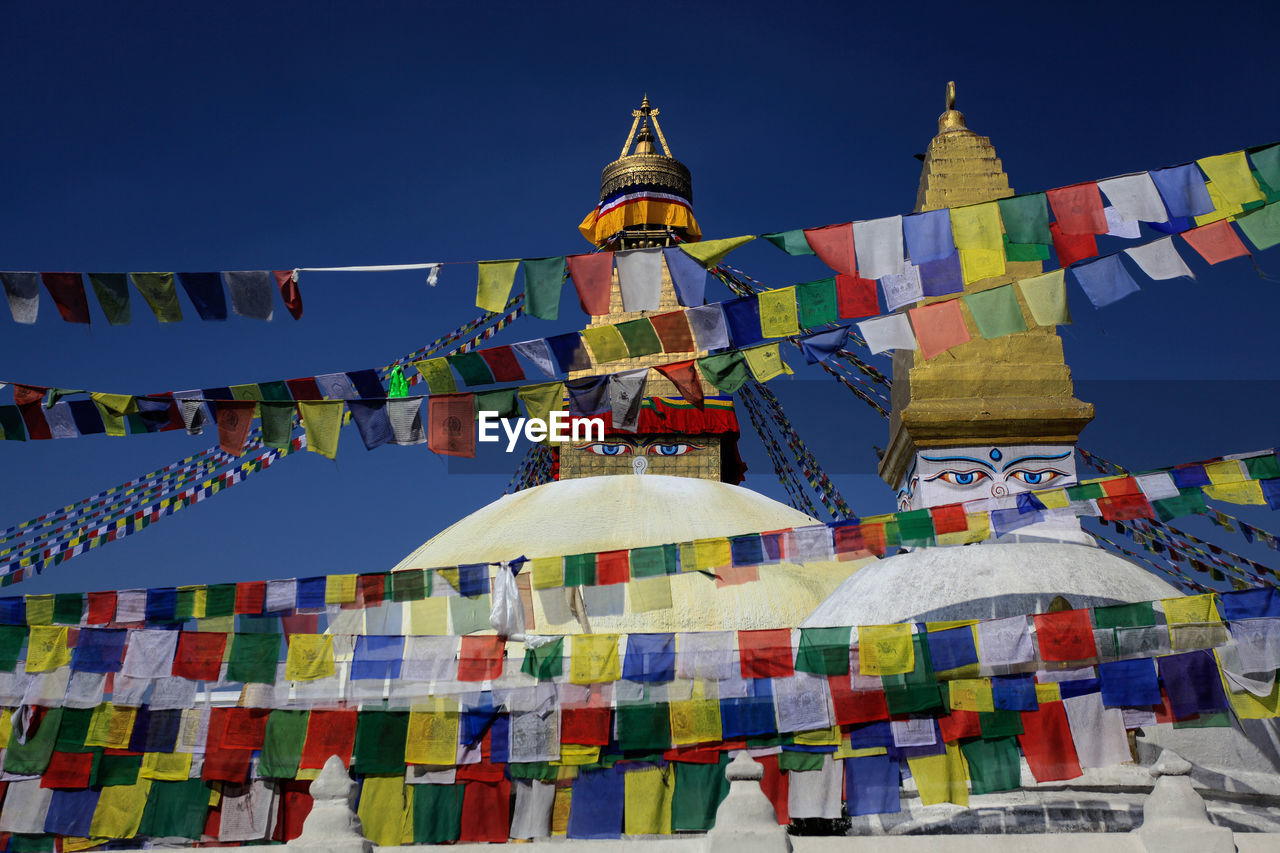 Low angle view of prayer flags and temples at boudhanath against clear sky