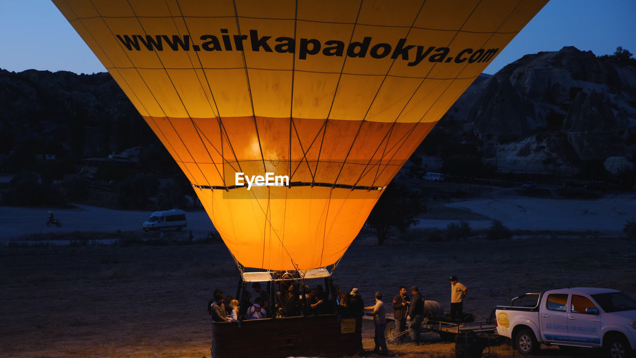vehicle, hot air balloon, transportation, aircraft, mode of transportation, air vehicle, hot air ballooning, balloon, travel, adventure, nature, car, mountain, travel destinations, sky, environment, land vehicle, land, vacation, trip, motor vehicle, holiday, scenics - nature, tourism, journey, flame, group of people, twilight, landscape, fire, executive car, outdoors, dusk, burning, leisure activity, night, flying, water, evening, nautical vessel, sea
