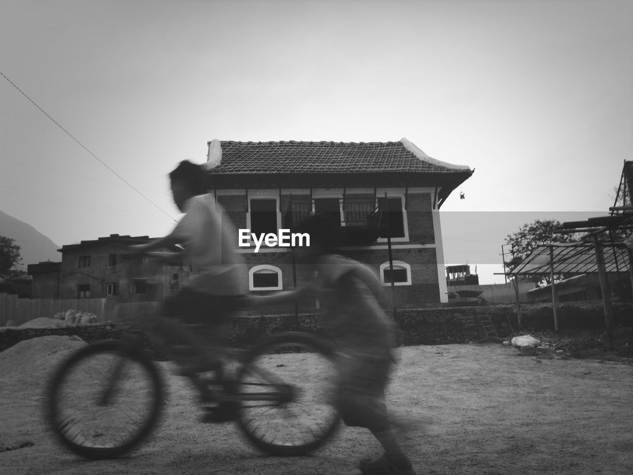 Side view of blurred boys bicycling against house