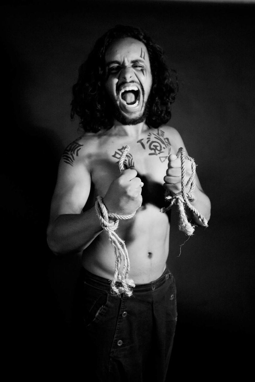 Portrait of aggressive shirtless man with ropes tied on hands against wall