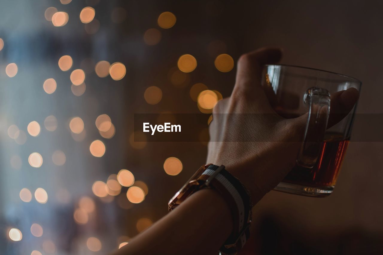 Close-up of human hand holding drink against illuminated lights at night