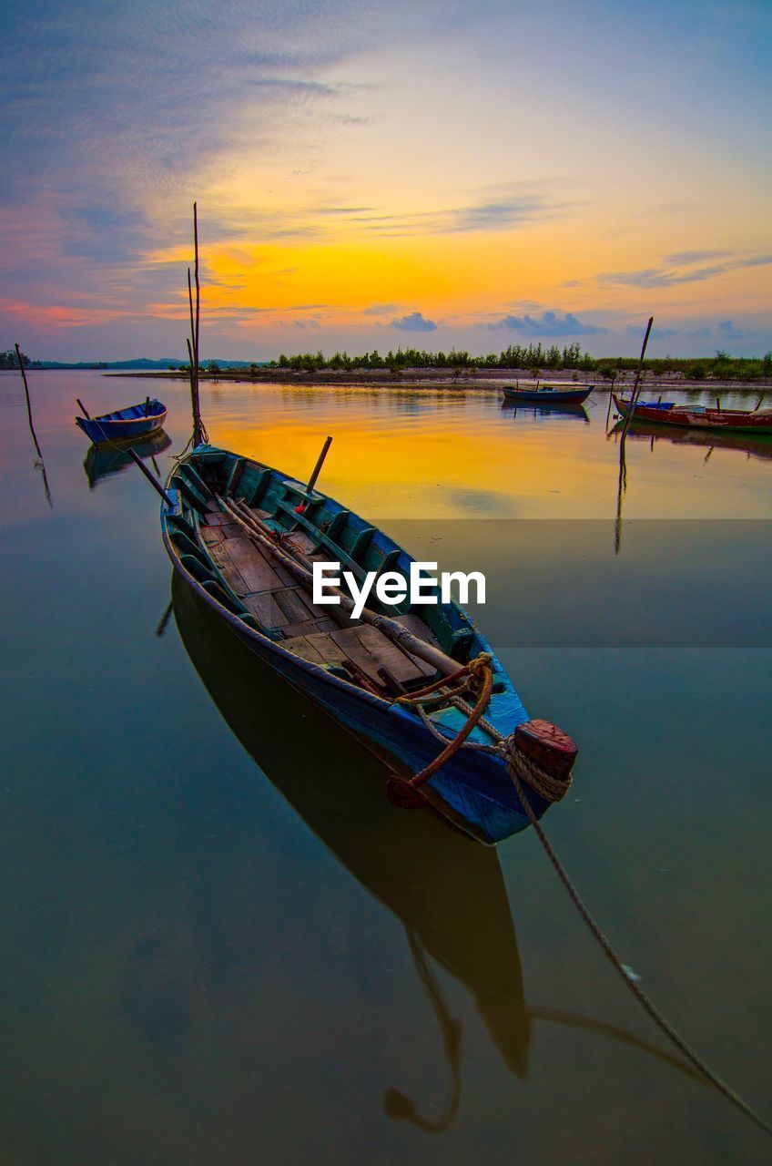 Boat moored in lake against sky during sunset