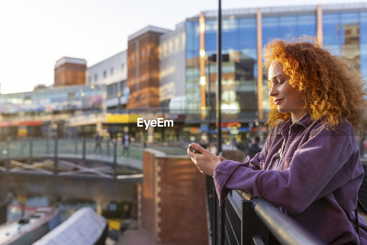 Uk, birmingham, redhead woman using smartphone in the city at sunset