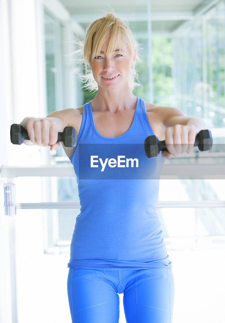 Portrait of confident woman exercising with dumbbell in gym