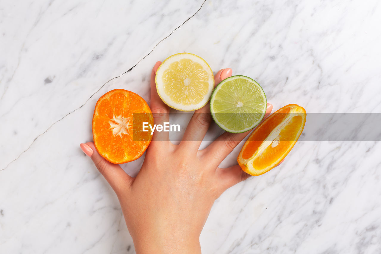 CROPPED IMAGE OF HAND HOLDING ORANGE SLICE