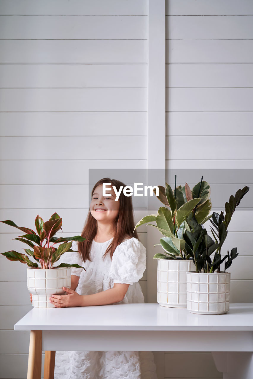 portrait of smiling young woman sitting on table against wall