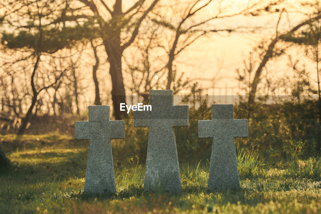 Three catholic stone crosses on green grass at sunset in german military cemetery in europe