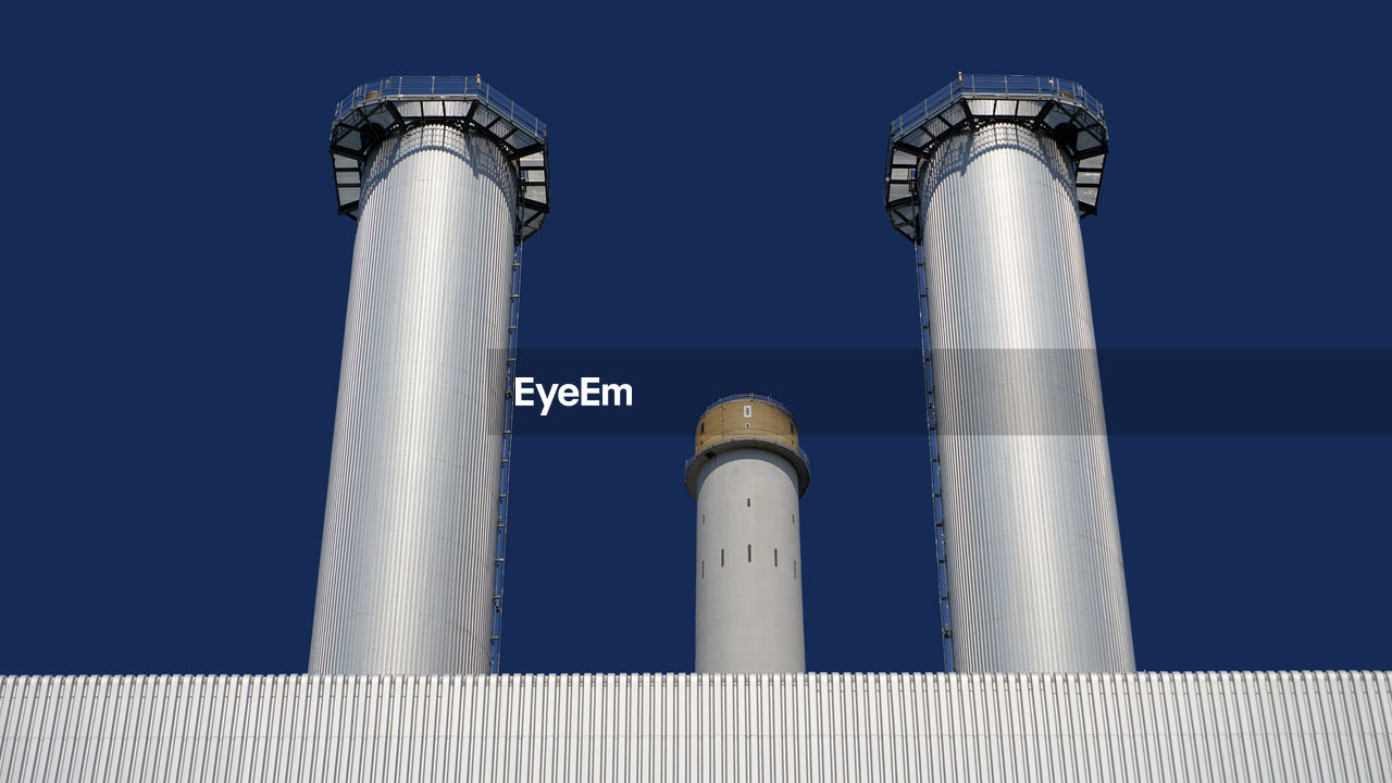 Low angle view of smoke stacks against clear blue sky