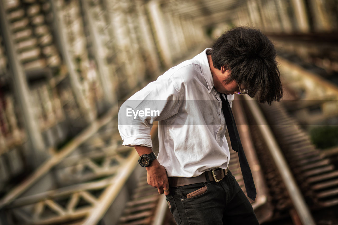 Young man looking down while standing on railroad track