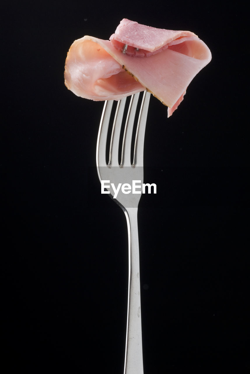 Close-up of meat in fork against black background