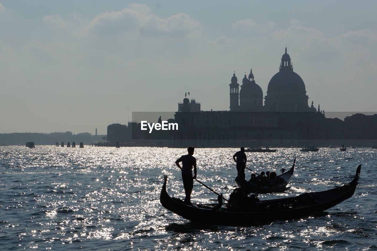 Silhouette gondoliers sailing in grand canal by basilica santa maria della salute