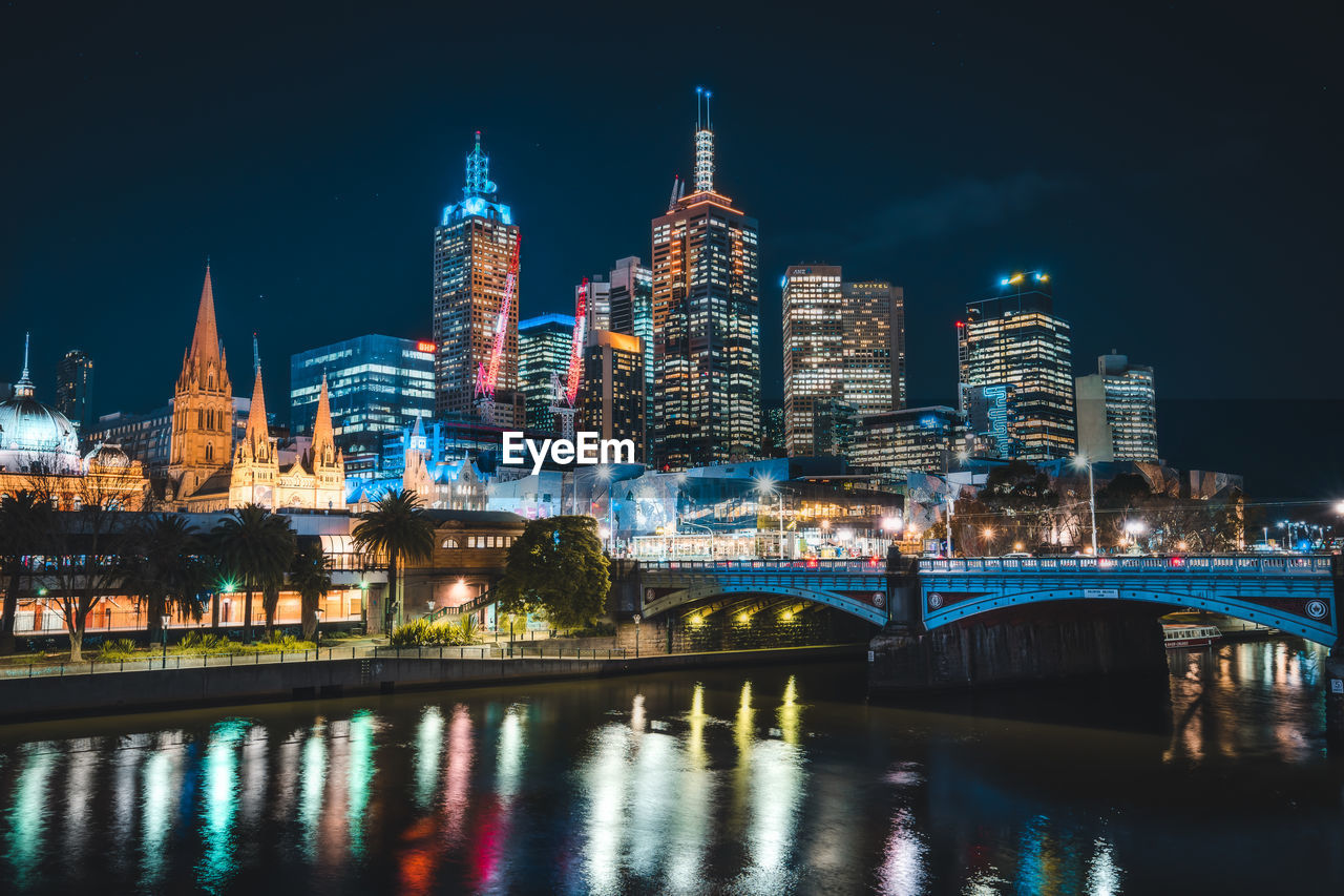 Illuminated buildings by river against sky in city at night