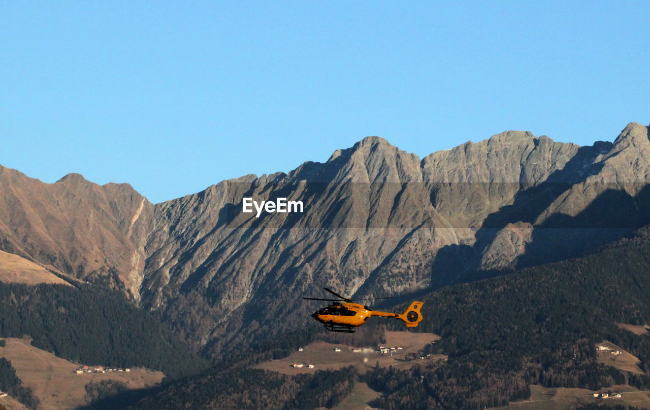 Helicopter flying over rocky mountains against clear sky