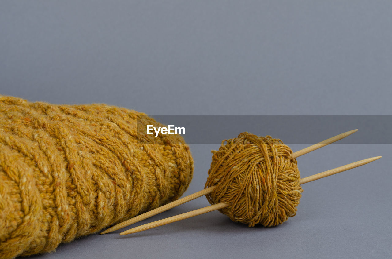 Yellow yarn ball with bamboo knitting needles and knitted cables scarf on gray background.