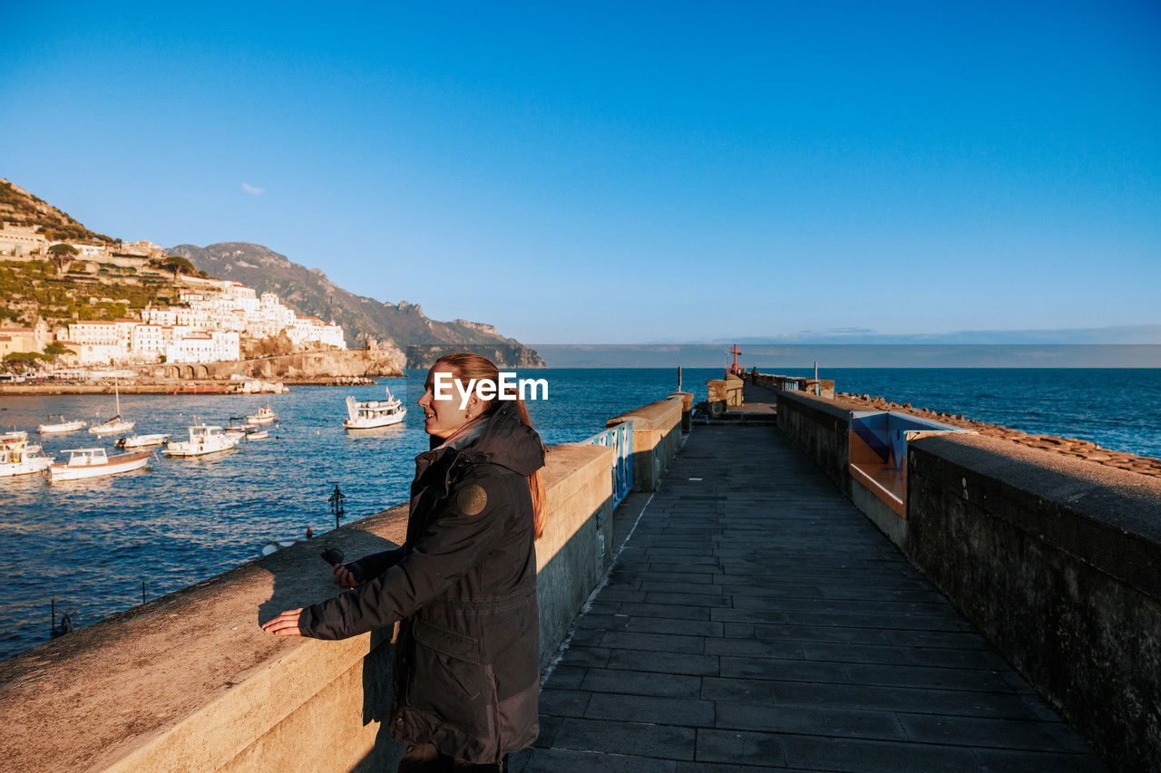 rear view of woman standing on pier over sea against clear blue sky