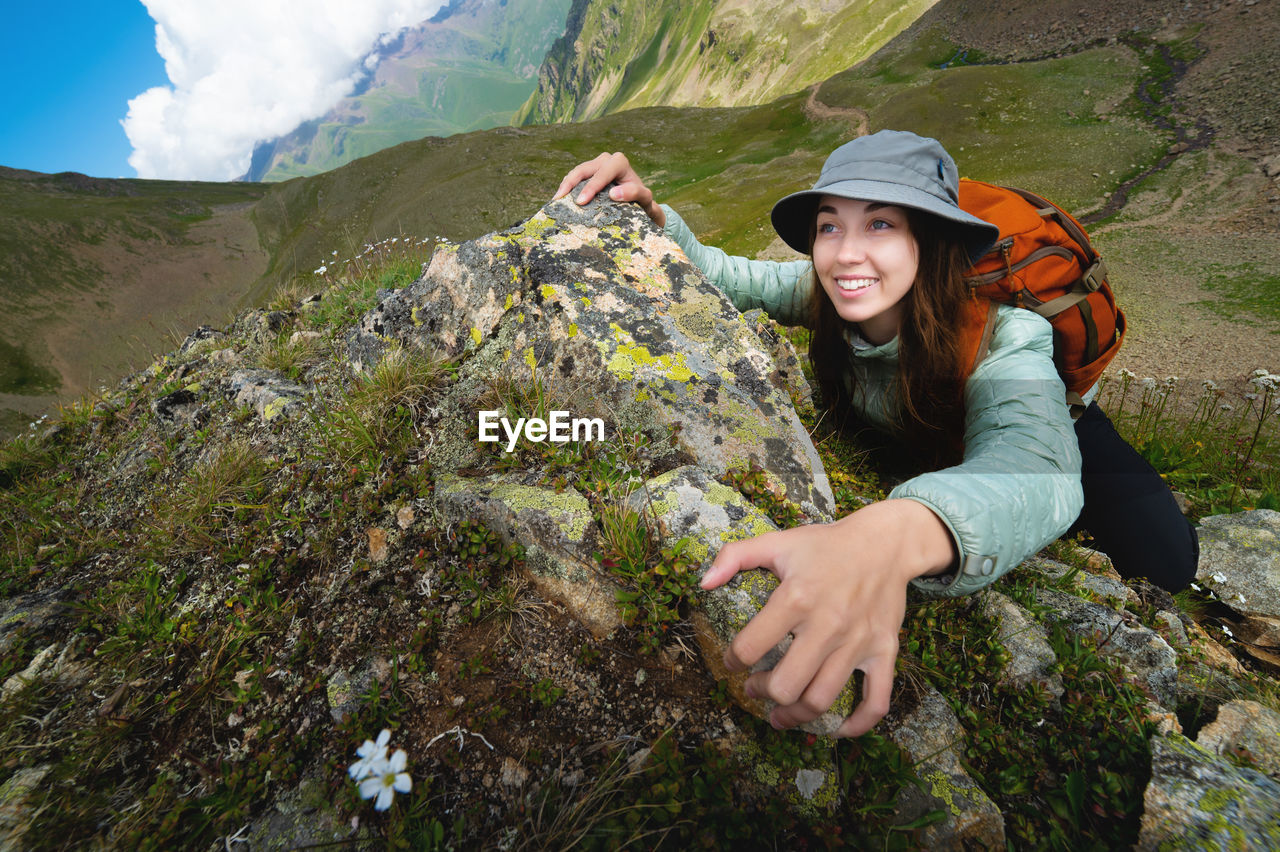 Young tourist woman smiles and climbs to the top of the cliff with a backpack. climbing a steep
