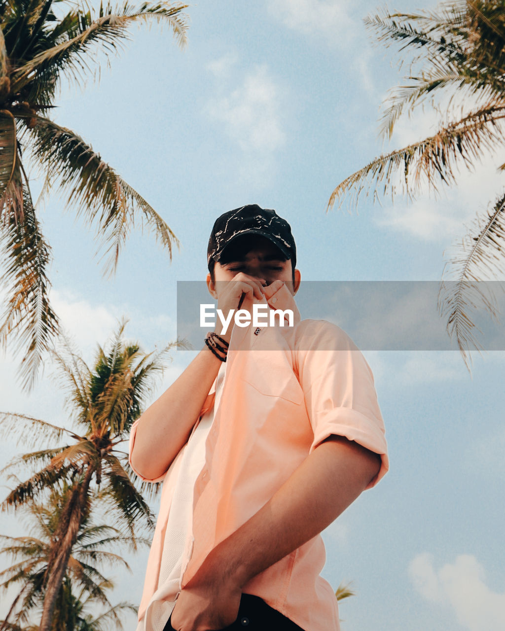 LOW ANGLE VIEW OF WOMAN STANDING ON PALM TREE