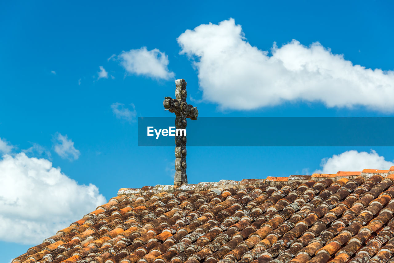 Low angle view of cross over roof tiles against sky