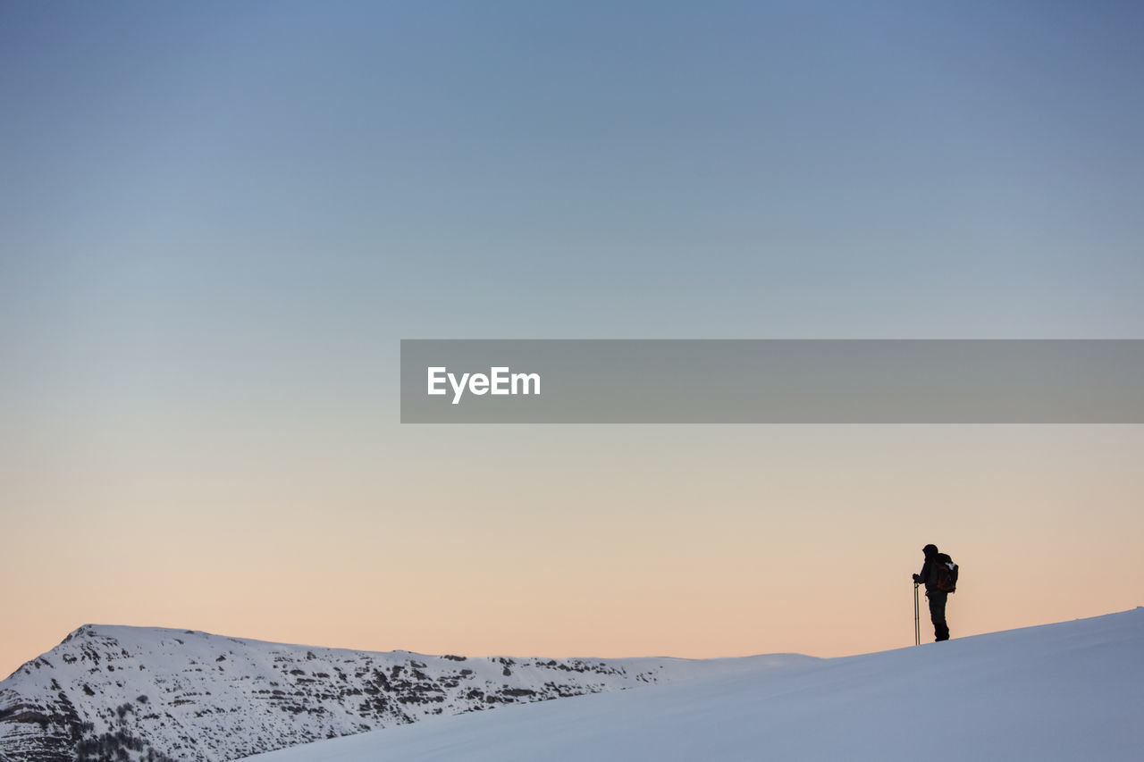 Man standing on snowcapped mountain against clear sky at sunset