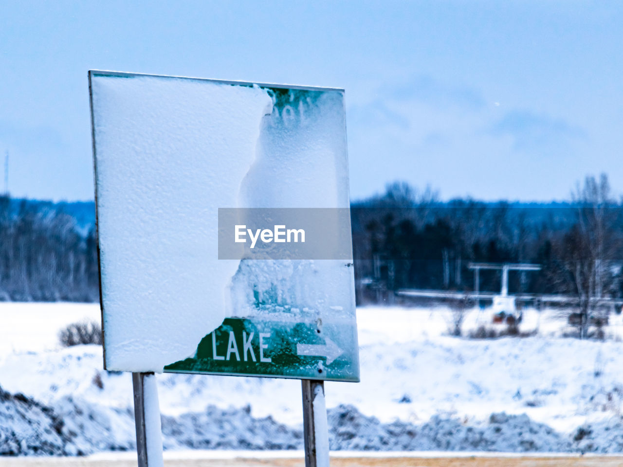 Highway exit sign points towards a lake, but its name is obscured by snow