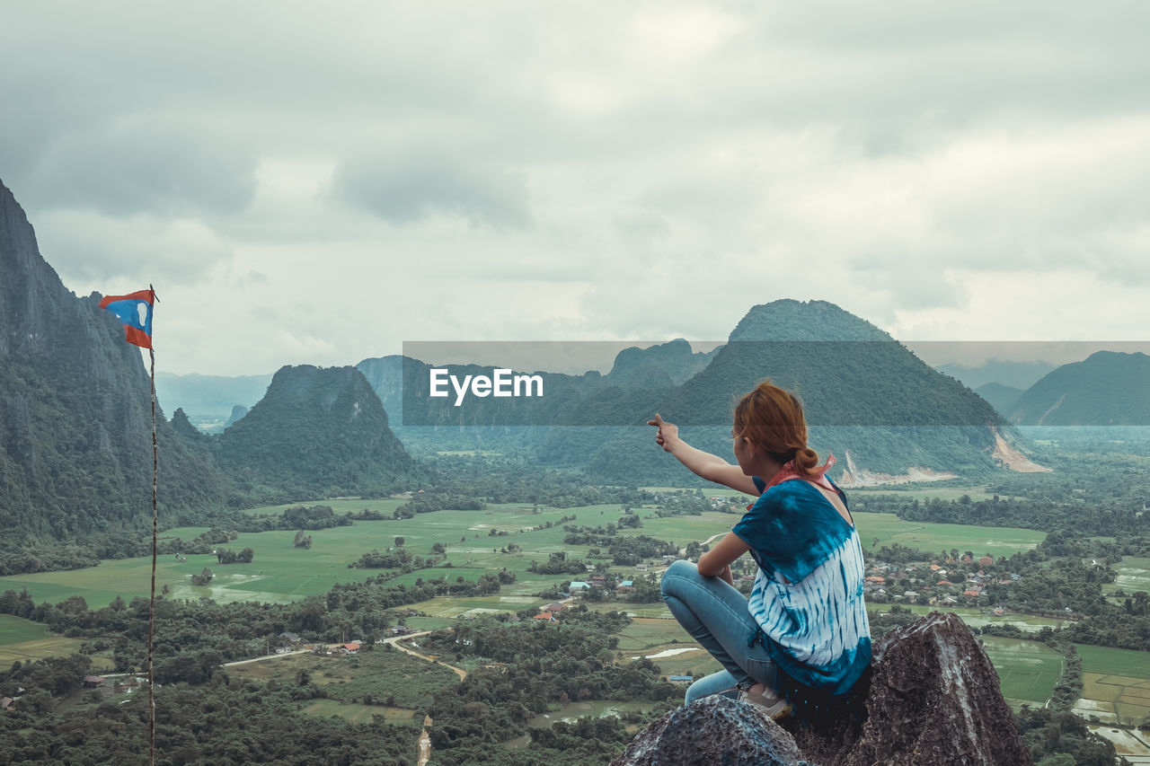 Side view of mid adult woman pointing at flag against mountains