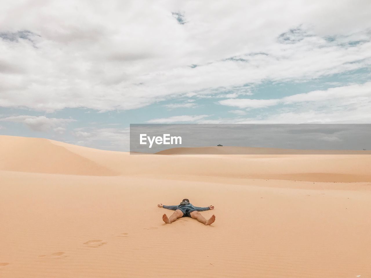 Man lying at desert against cloudy sky