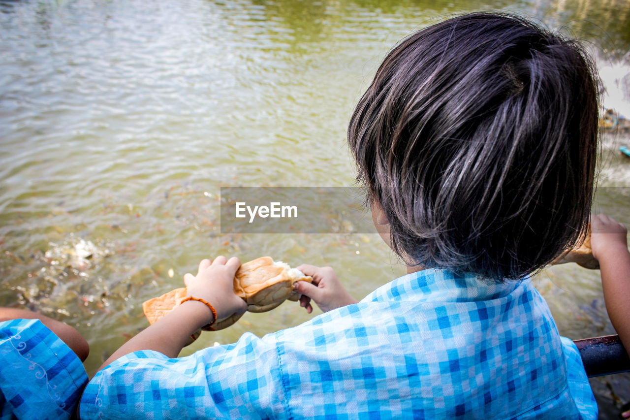 High angle view of boy eating bread while sitting in boat on lake