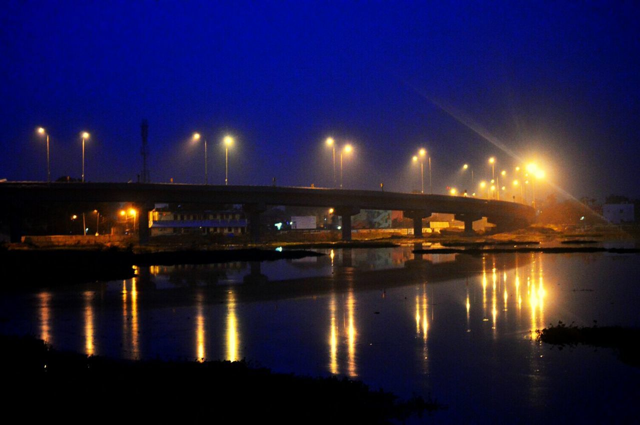 ILLUMINATED BRIDGE OVER RIVER AT NIGHT