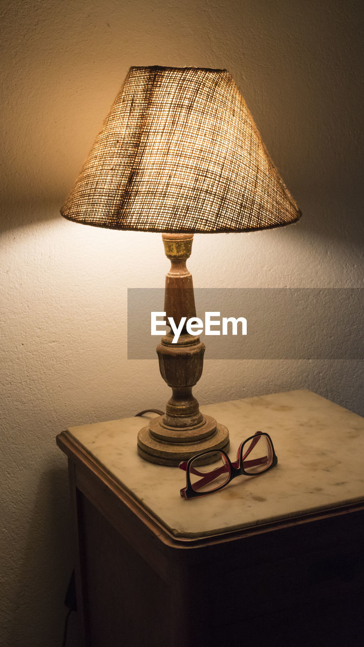 Illuminated electric lamp by eyeglasses on table