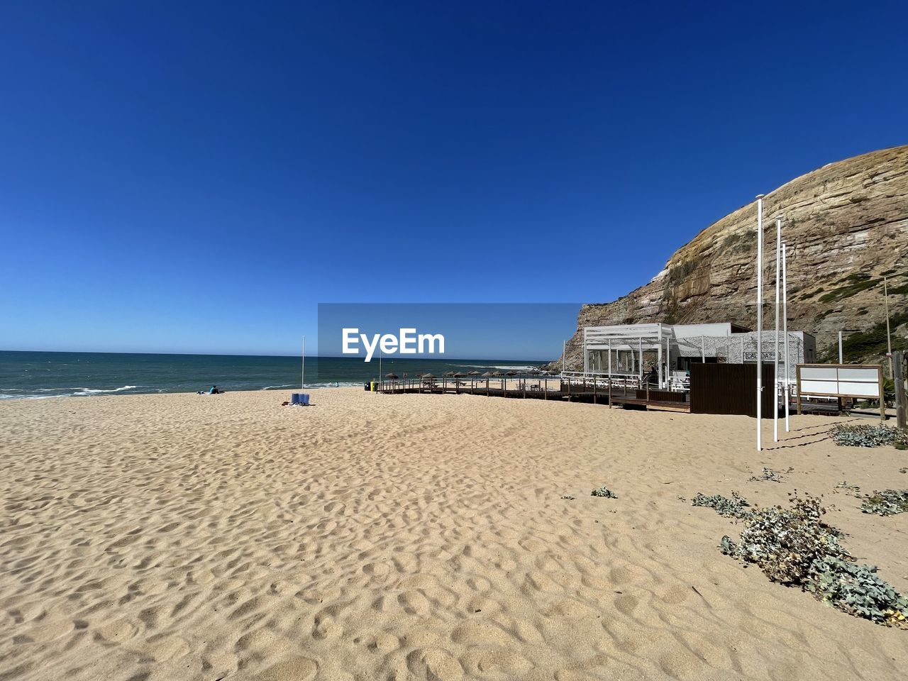 land, beach, sky, sea, sand, water, clear sky, nature, blue, scenics - nature, beauty in nature, ocean, travel destinations, holiday, sunny, shore, tranquility, architecture, coast, horizon over water, vacation, trip, horizon, travel, hut, body of water, tranquil scene, day, built structure, no people, tourism, summer, sunlight, outdoors, copy space, coastline, building exterior, sand dune, landscape, natural environment, idyllic, environment, dune, non-urban scene