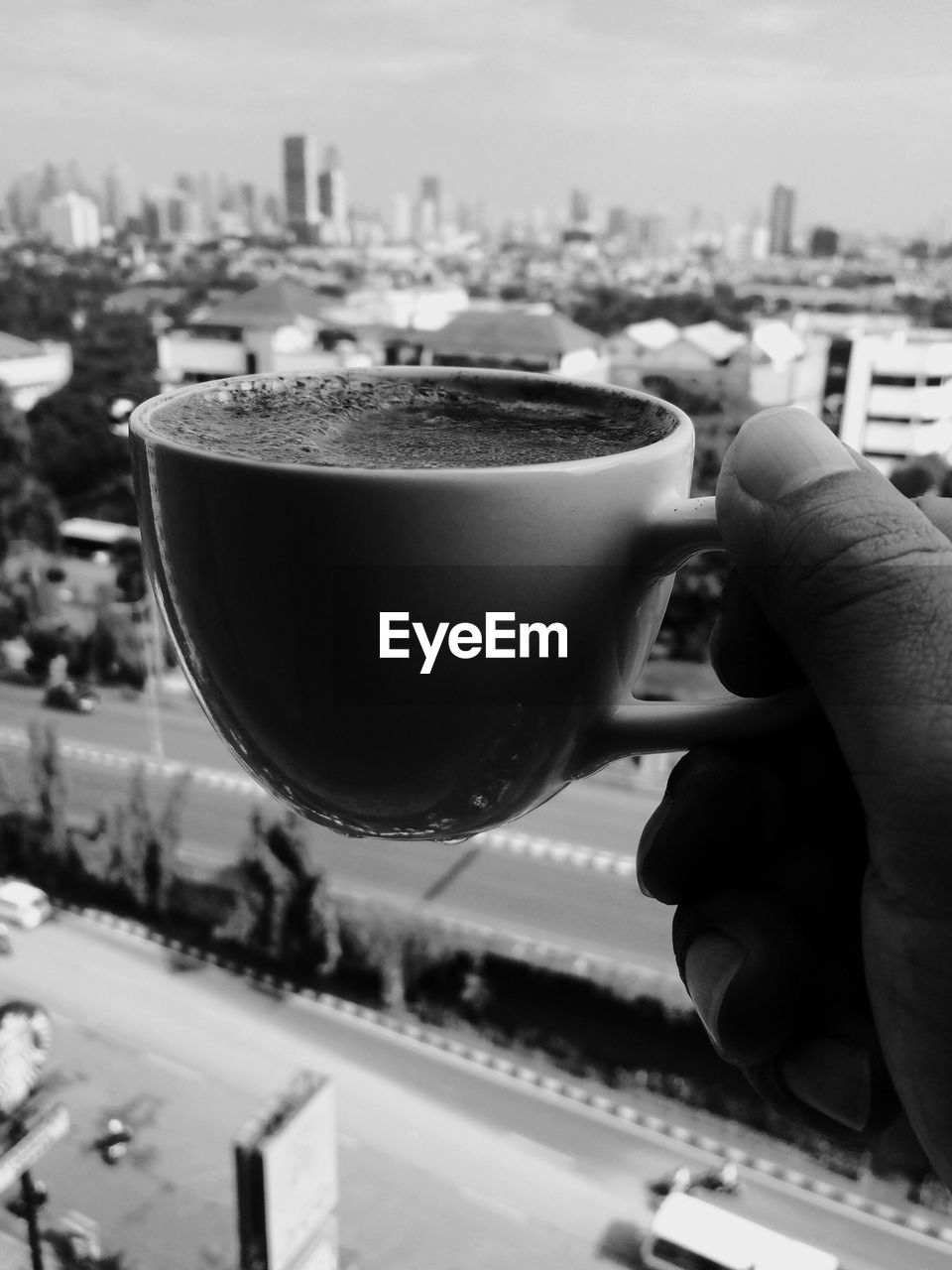 CLOSE-UP OF HAND HOLDING COFFEE CUP AGAINST CITYSCAPE