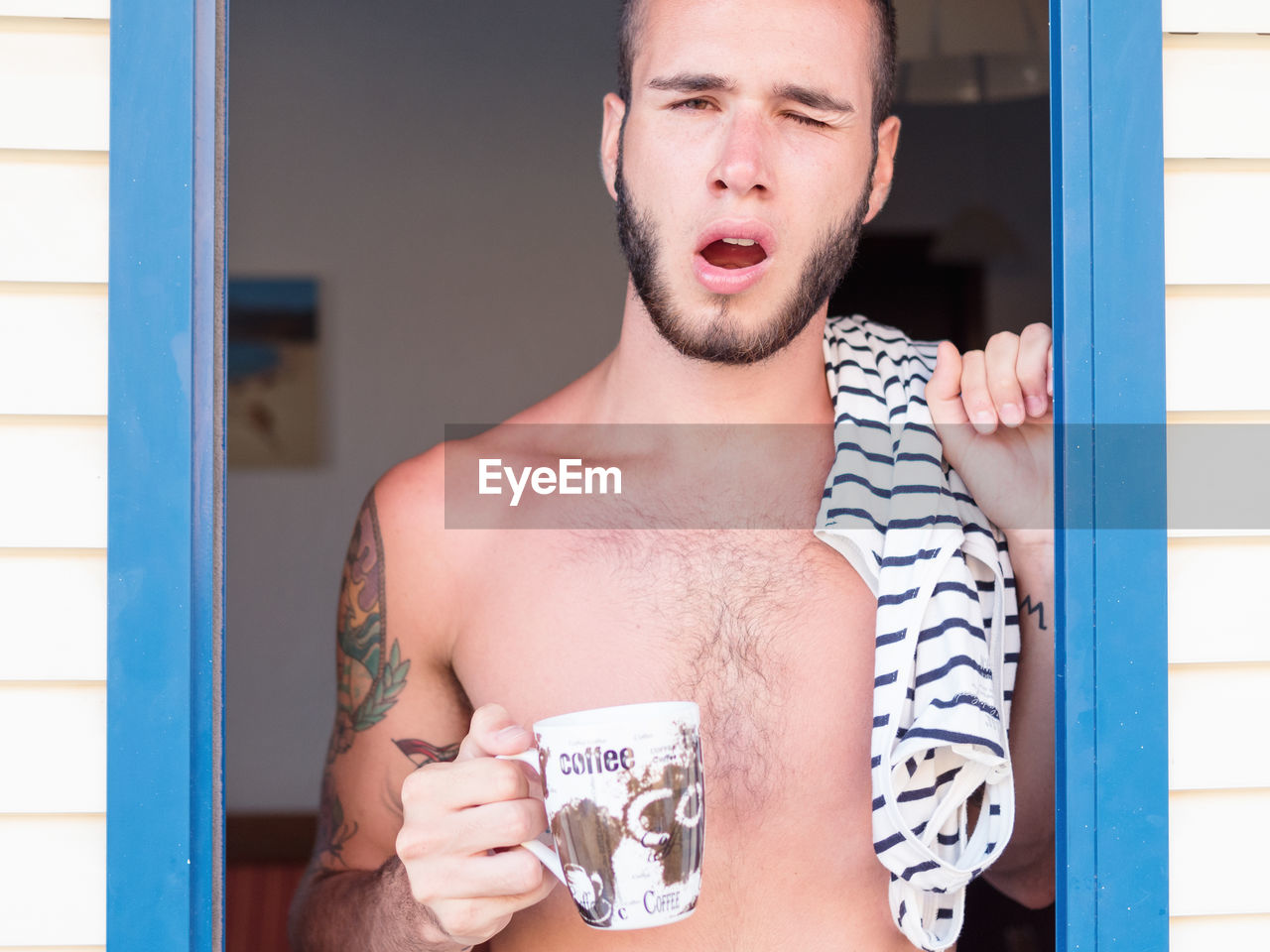 Close-up portrait of man winking while having coffee standing at doorway